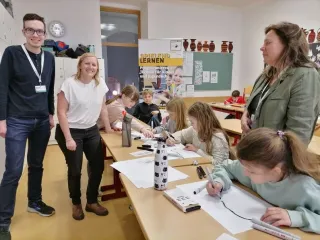 Kinder lernen mit Ozobots programmieren, die Mentor:innen posieren für die Kamera