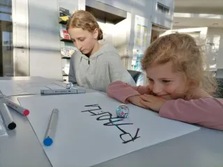 Zwei Mädchen schauen auf Miniroboter, die entlang von Linien fahren.